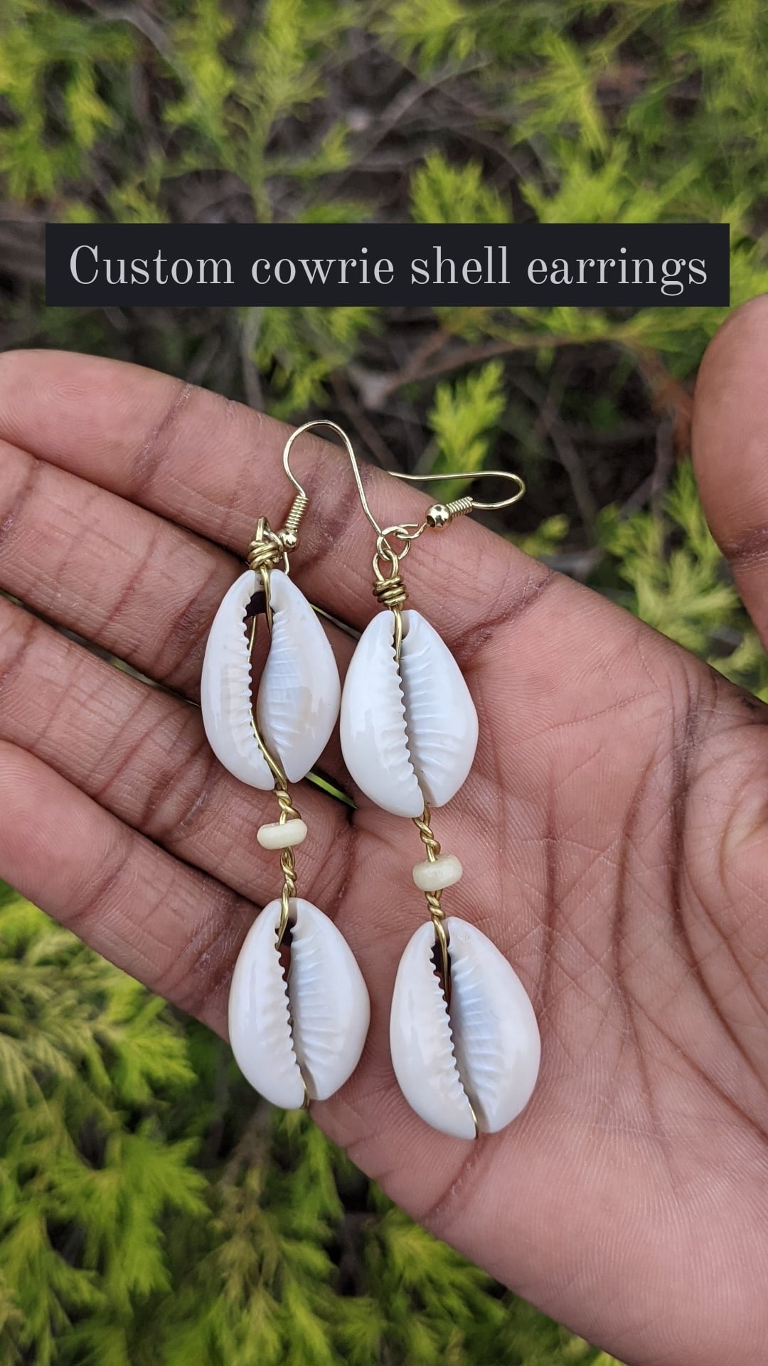 A photo of two pairs of handcrafted cowrie shell earrings being held by a person