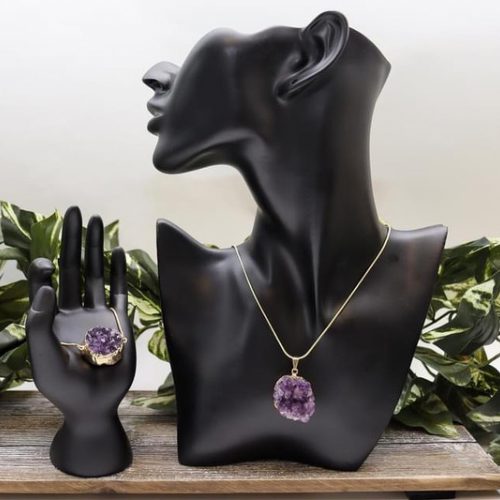 A photo of an amethyst druzy pendant around a mannequin's neck with an amethyst druzy bracelet being held in a mannequin's hand