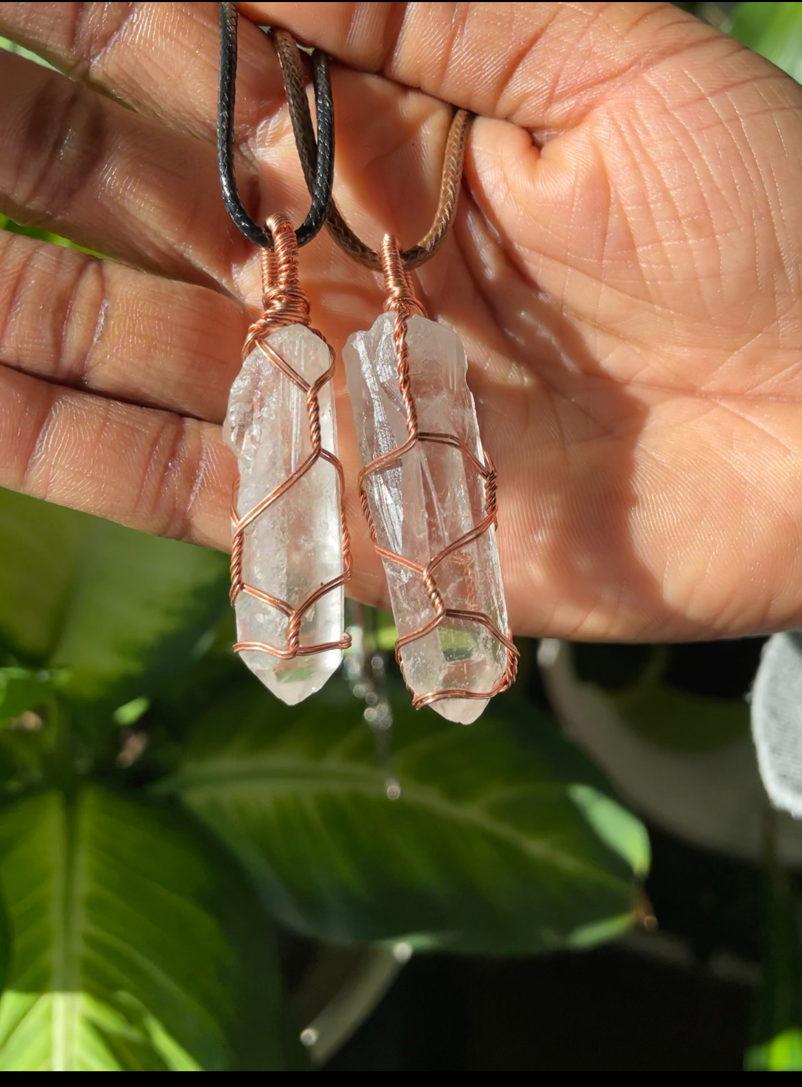 A photo of a handcrafted clear quartz pendant being held by a person