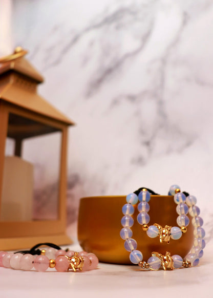 A photo of a blue elephant bracelet laying in a cup and a pink elephant bracelet laying on a table