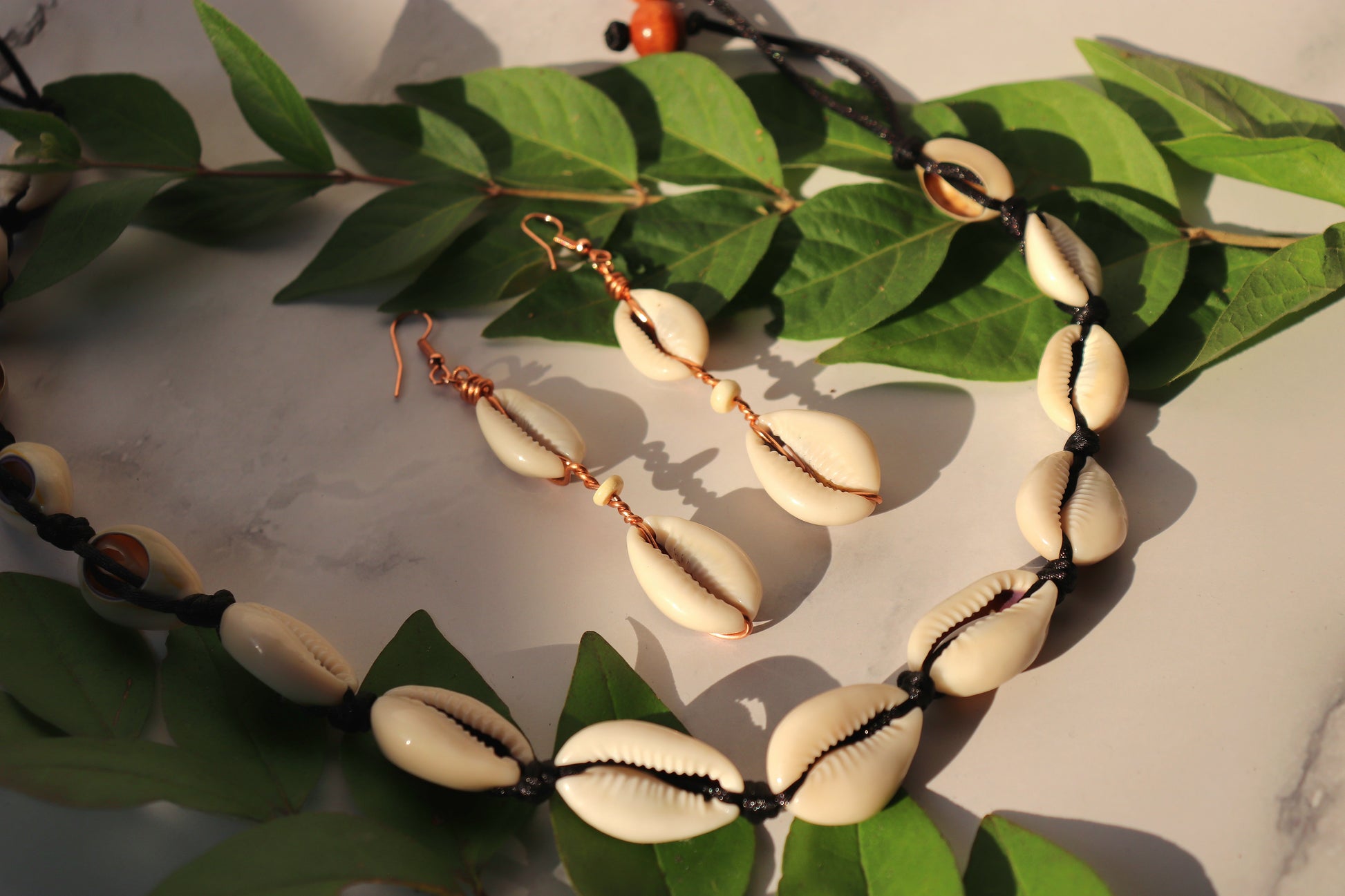 A photo of two handcrafted cowrie shell earrings and a necklace laying on a table