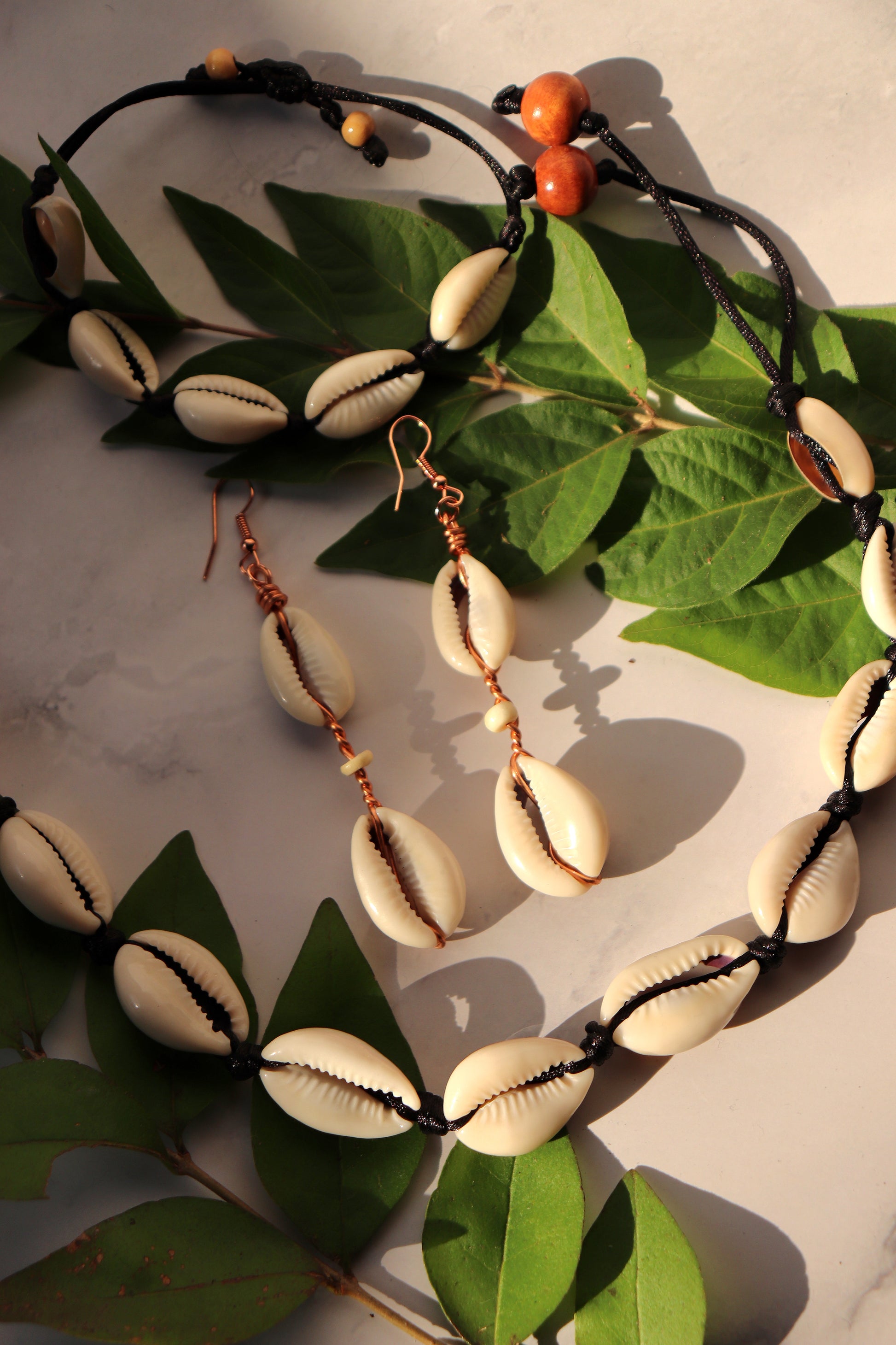 A photo of two handcrafted cowrie shell earrings, one bracelet, and one necklace laying on a table